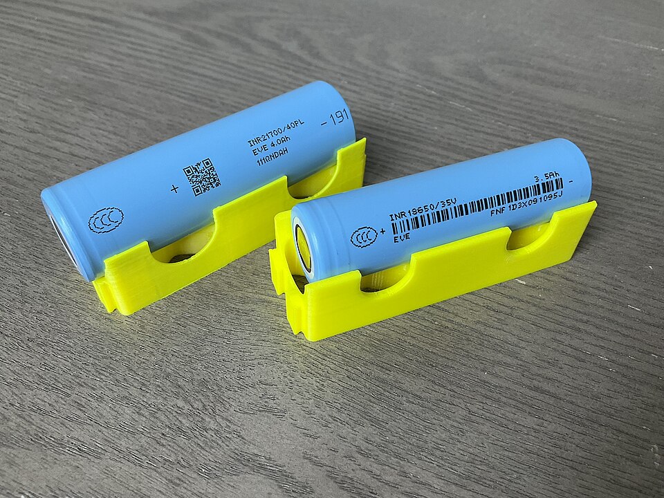Two cylindrical lithium-ion battery cells of different industrial sizes on a dark surface