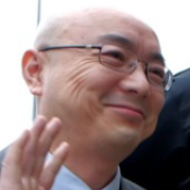 Portrait of Mo Hailong smiling and raising one hand